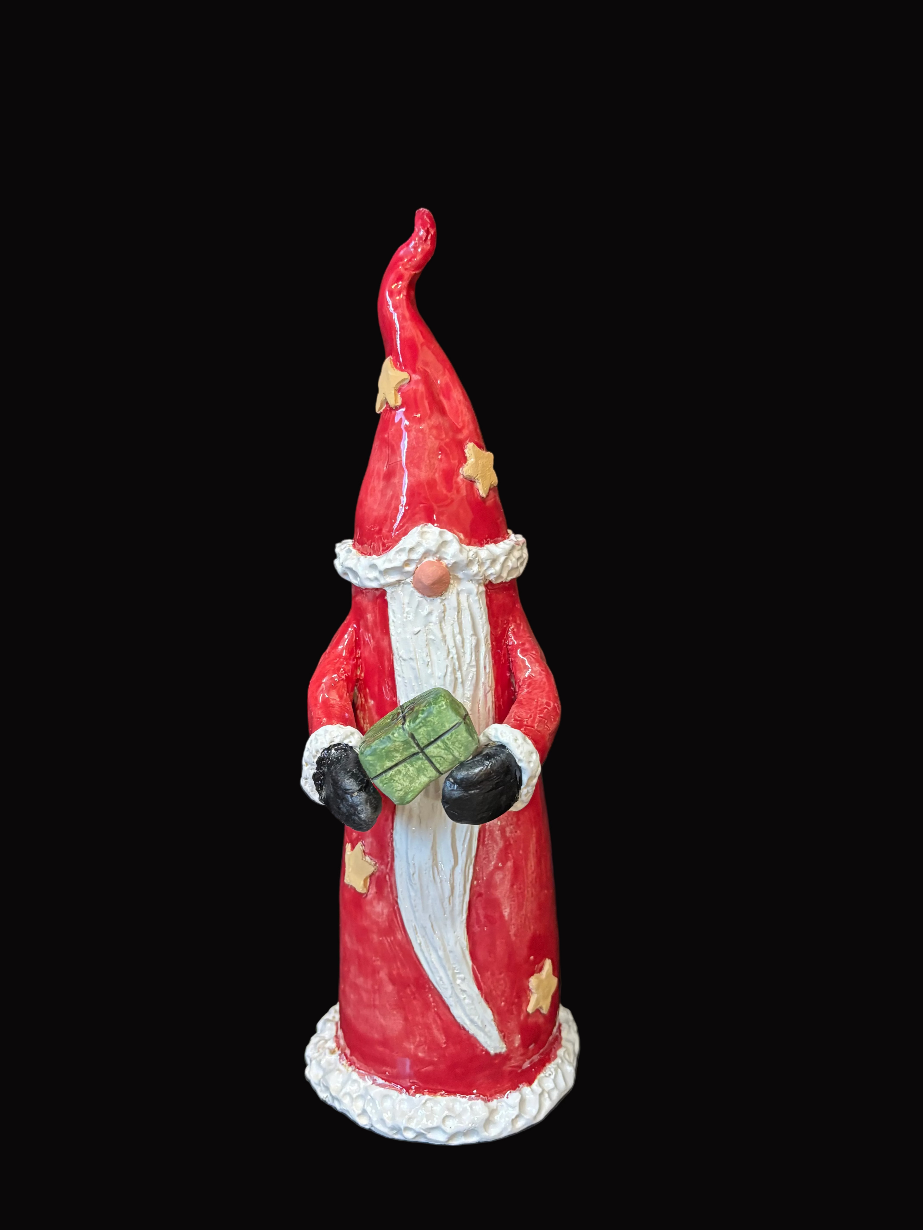 Red gnome figurine with a white beard holding a green box on a dark surface.