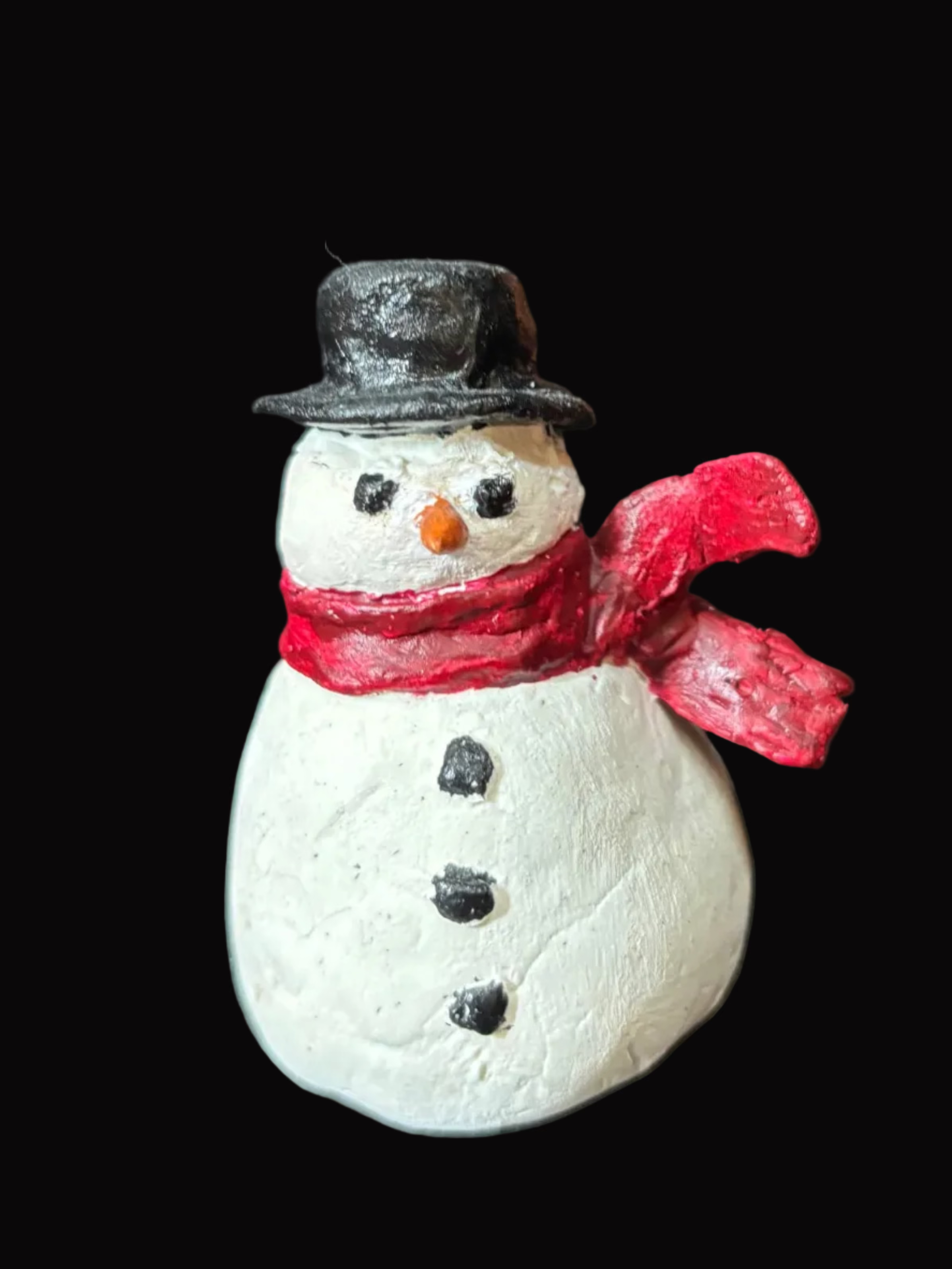 Small snowman figurine with a red scarf and black top hat on a black background