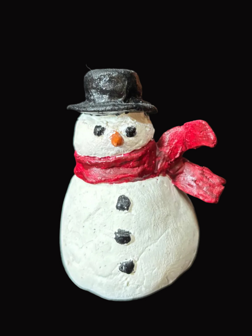 Small snowman figurine with a red scarf and black top hat on a black background